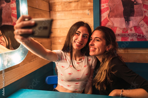 Dos amigas tomándose selfies en un bar decorado con temática circense photo