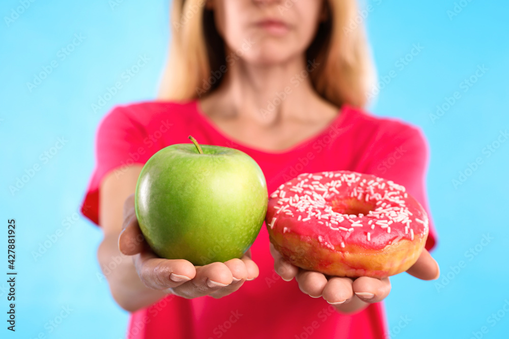 Woman choosing between doughnut and fresh apple on light blue background, closeup Woman choosing between doughnut and fresh apple on light blue background, closeup