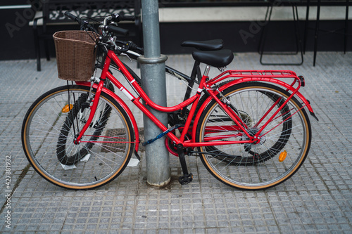 Bicicleta roja atada a un poste junto a otra bicicleta negra