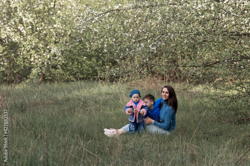 a mother with her children sits on the grass in a blooming apple orchard