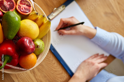 Nutritionist, dietitian woman writing a diet plan, with healthy vegetables and fruits