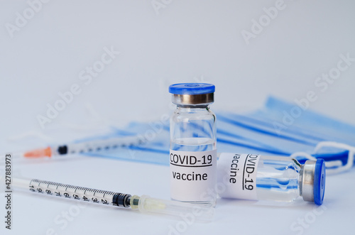 Creative ideas of vaccination concept. Top view of syringe with medical masks and vaccine vial glass bottles for vaccination against COVID-19. Coronavirus pandemic. Copy space. 