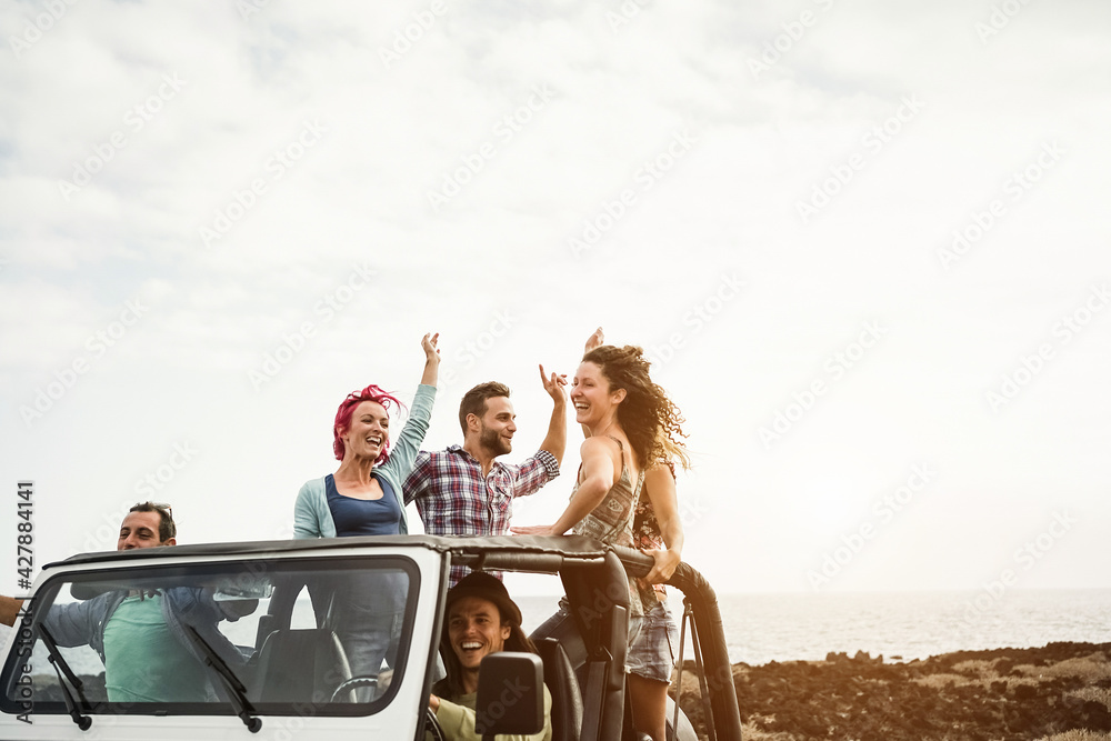 Group of happy friends doing excursion on beach in convertible 4x4 car- Soft focus on top man face - obrazy, fototapety, plakaty 