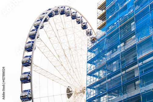 Large modern spinning ferris wheel stands next to a building construction site in a blue protective cover next to the town s new buildings in Dresden  Germany. Architecture and travel concept