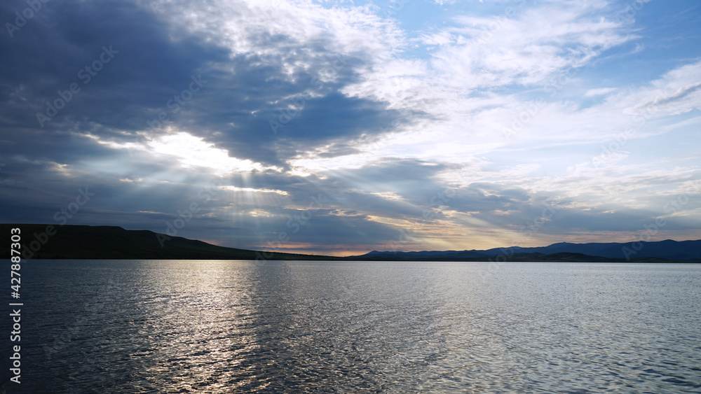 Sunset on the lake before a thunderstorm. Dramatic sky. Reflection of sunlight in water. Ripples. Beautiful waterscape background. Sunset on the lake before a thunderstorm. Dramatic sky. Reflection of sunlight in water. Ripples. Beautiful waterscape background.