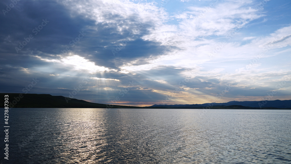 Sunset on the lake before a thunderstorm. Dramatic sky. Reflection of sunlight in water. Ripples. Beautiful waterscape background.