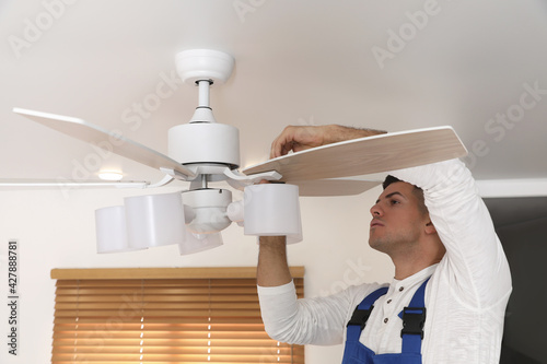 Electrician repairing ceiling fan with lamps indoors photo