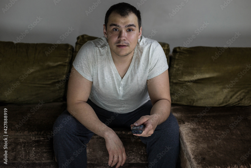 A man is watching TV. A man in home clothes at home on the couch with a remote control from the TV A man is watching TV. A man in home clothes at home on the couch with a remote control from the TV