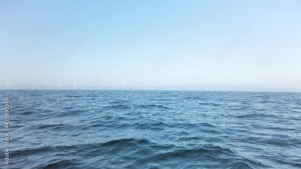 Windmill park at open sea, seen from a far distance. It is a beautiful, clear, sunny spring day. Filmed from a boat. Location is Øresund between Copenhagen and Malmo. Slow motion 4K Windmill park at open sea, seen from a far distance. It is a beautiful, clear, sunny spring day. Filmed from a boat. Location is Øresund between Copenhagen and Malmo. Slow motion 4K