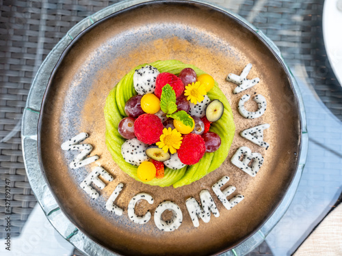 Mixed fruit, watermelon, melon, avocado, kiwi, strawberry, blueberry, dragon fruit, raspberry, decorated on dish with carving 'Welcome Back' 
