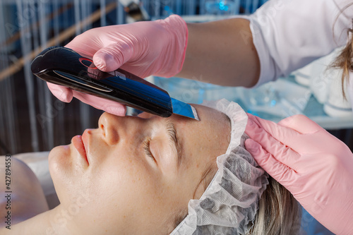A professional cosmetologist performs an ultrasonic face cleaning procedure for a woman.