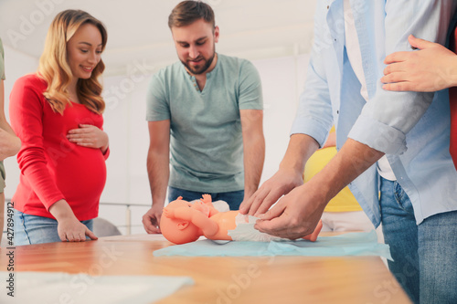 Future fathers and pregnant women learning how to swaddle baby at courses for expectant parents indoors, closeup photo