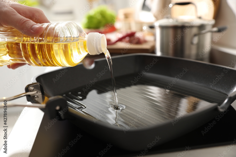 Man pouring cooking oil into frying pan in kitchen, closeup Man pouring cooking oil into frying pan in kitchen, closeup
