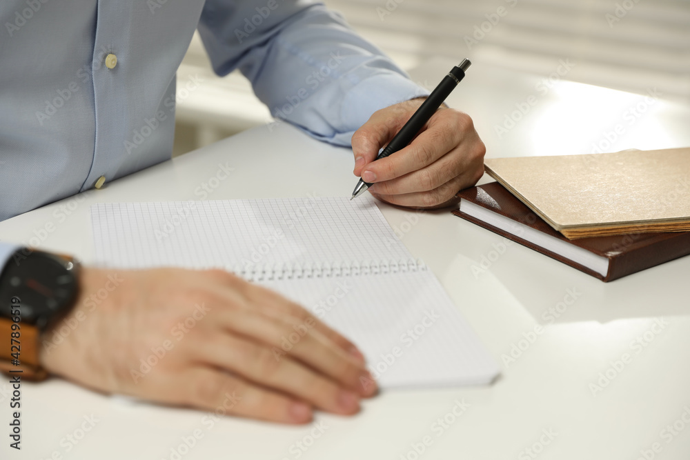 Left-handed man writing in notebook at white table, closeup Left-handed man writing in notebook at white table, closeup