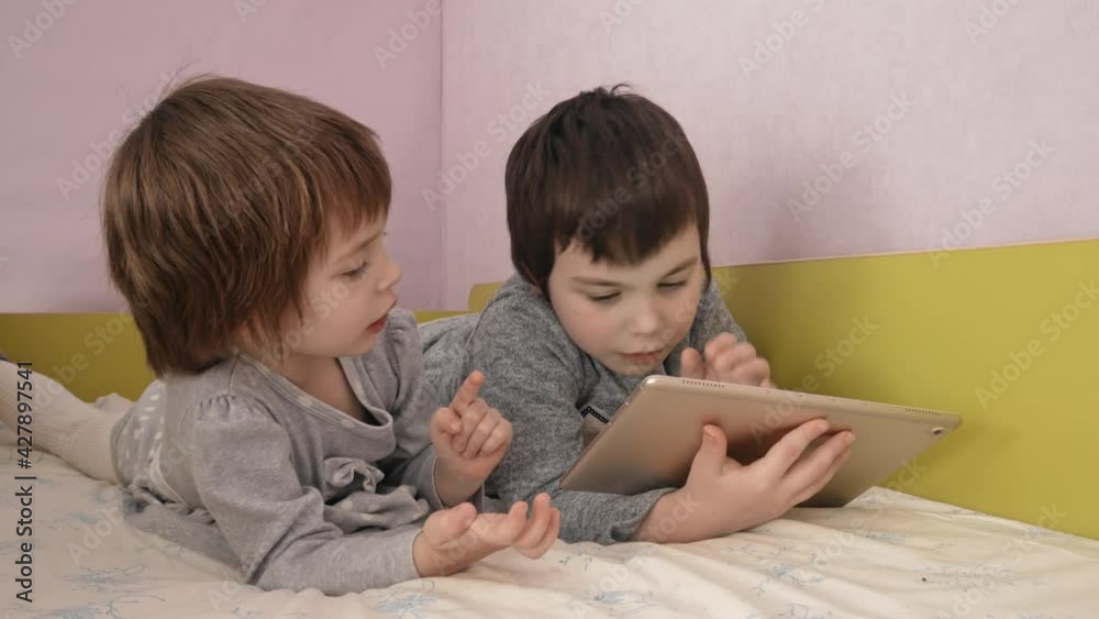 Children and gadget. Two girls are watching cartoons on a tablet. Two girls in gray dresses are playing a computer game. Children and gadget. Two girls are watching cartoons on a tablet. Two girls in gray dresses are playing a computer game.