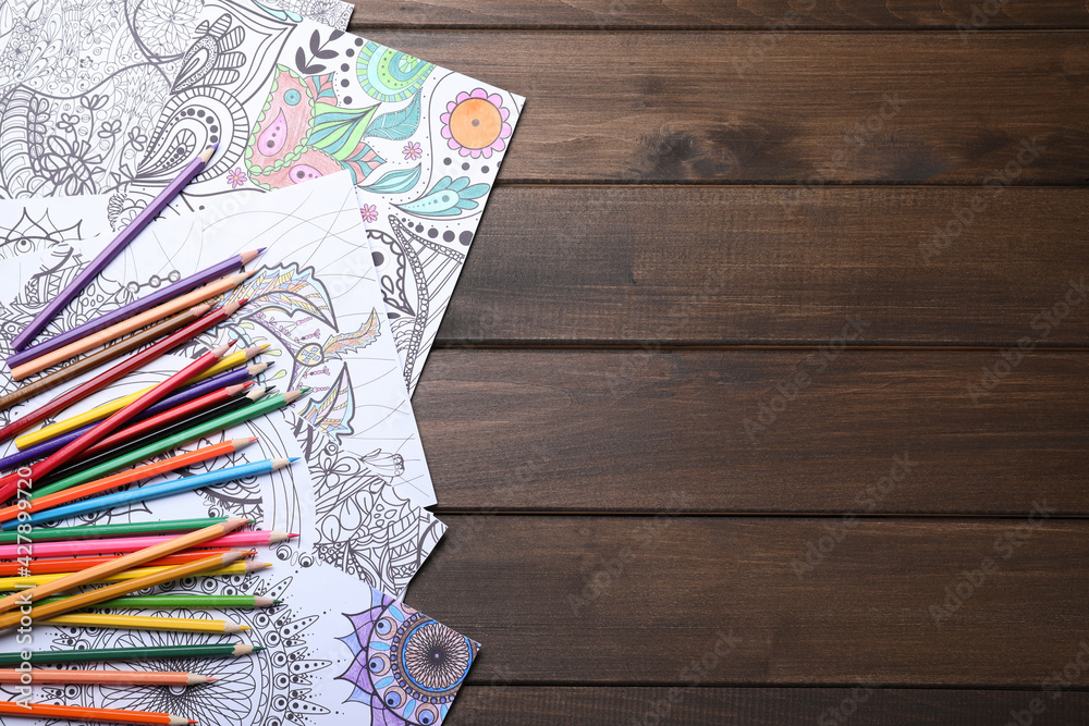 Antistress coloring pages and pencils on wooden table, flat lay. Space for text