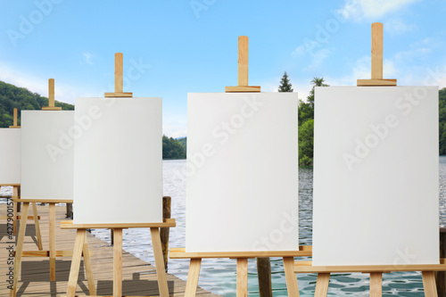 Wooden easels with blank canvases near river on sunny day