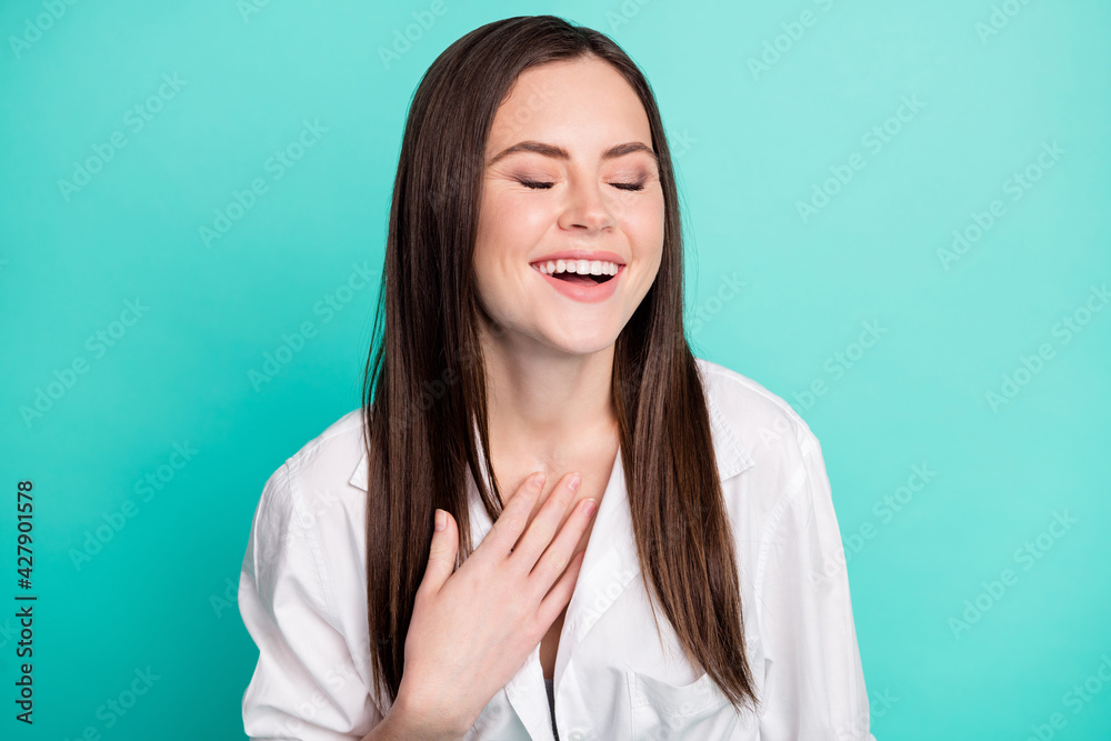 Photo of cheerful funky young woman hold hand chest laugh funny joke humor isolated on teal color background Photo of cheerful funky young woman hold hand chest laugh funny joke humor isolated on teal color background