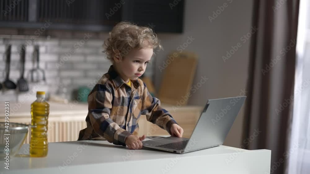 toddler alone at home, baby boy is using laptop on home kitchen, viewing cartoons, happy little child