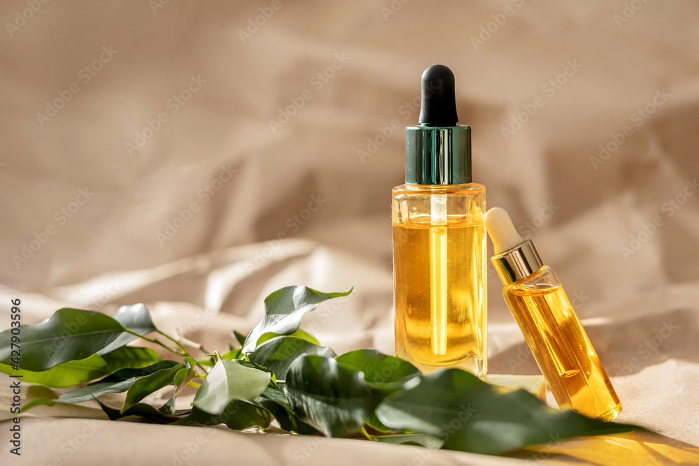 Glass dropper bottles with cosmetic oil, essential or serum and green leaves on paper background. Concept of natural organic spa cosmetics. Herbal homeopathic products. Branding mockup. Copy space. Glass dropper bottles with cosmetic oil, essential or serum and green leaves on paper background. Concept of natural organic spa cosmetics. Herbal homeopathic products. Branding mockup. Copy space.
