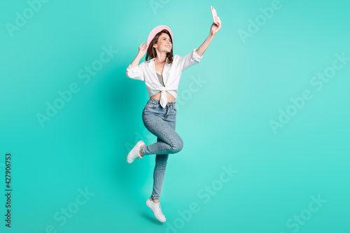 Photo of sweet cute young woman dressed white shirt cap tacking selfie modern device jumping isolated teal color background