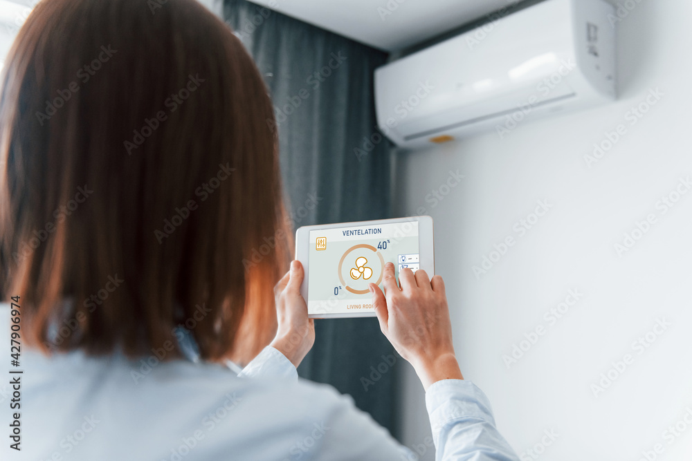 Modern technologies. Rear view of woman that is indoors controlling smart home Modern technologies. Rear view of woman that is indoors controlling smart home