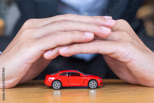Businessman hand cover or protection red car toy on table. Financial, money, refinance and Car insurance concept