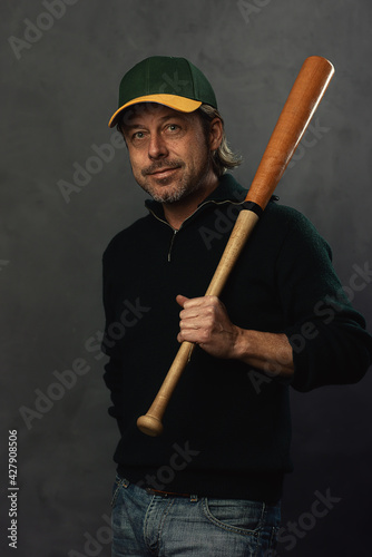Photography Smiling blond man with baseball cap and bat in a dark green wool sweater