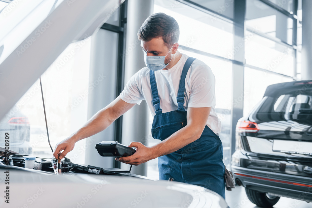 Young man in white shirt and blue uniform repairs automobile Young man in white shirt and blue uniform repairs automobile
