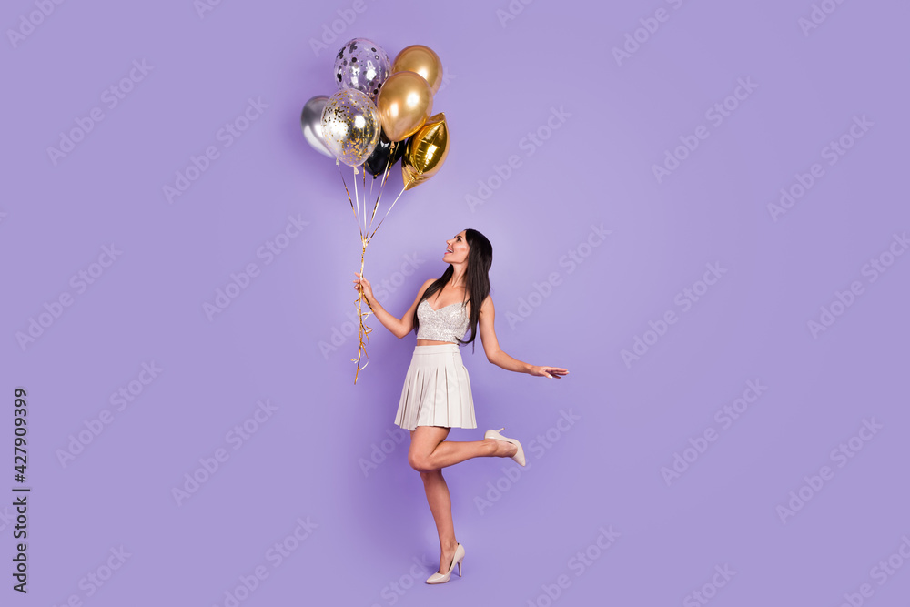 Full length profile side photo of cheerful lady look hold balloons prom party isolated on violet color background Full length profile side photo of cheerful lady look hold balloons prom party isolated on violet color background