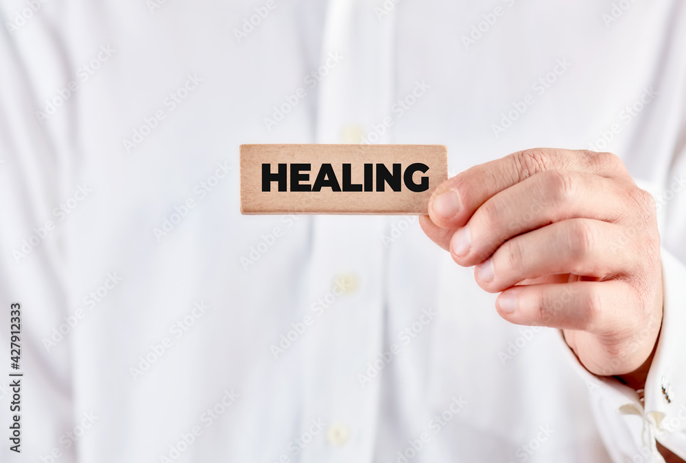 Male hand holds a wooden block with the message healing. Spiritual healing and mindfulness Male hand holds a wooden block with the message healing. Spiritual healing and mindfulness