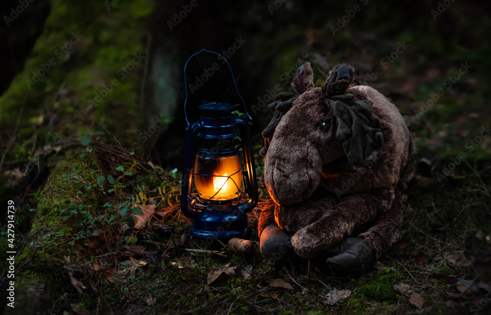A toy moose and kerosene lamp in the dark forest