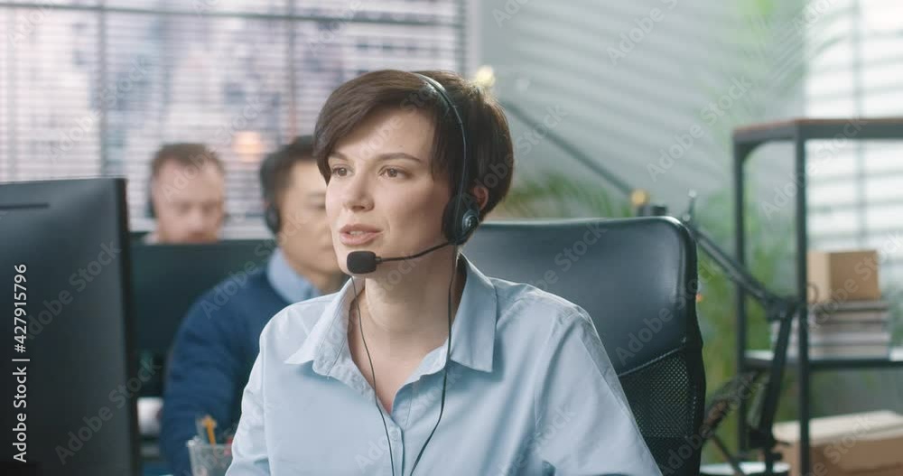 Beautiful woman with short stylish haircut working in call center and politely talks to client sitting in office at computer. Beautiful woman with short stylish haircut working in call center and politely talks to client sitting in office at computer.