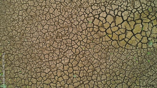 Top view of arid surface of earth. Shot. Arid terrain with clay soil and sparse grasses. Textured surface of dry earth with cracks