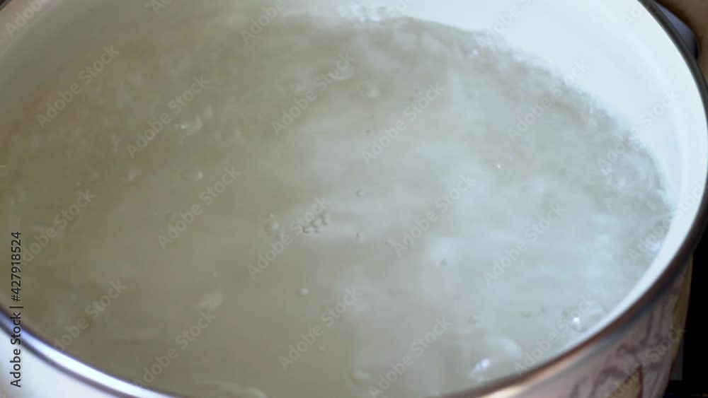 The water is boiling in a pot on the stove, the hot water is covered in bubbles. The water is boiling in a pot on the stove, the hot water is covered in bubbles.