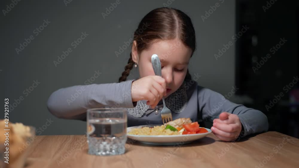 Little beautiful girl is eating in the kitchen. She sits on a chair at the table. The child eats pasta with a fresh salad of tomato, pepper and round cheese. 4K Little beautiful girl is eating in the kitchen. She sits on a chair at the table. The child eats pasta with a fresh salad of tomato, pepper and round cheese. 4K