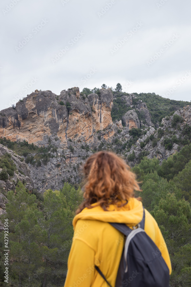 Naklejka premium Woman from behind with a yellow jacket hiking on a path in the mountains