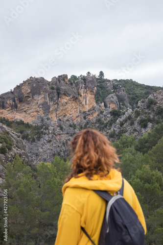 Woman from behind with a yellow jacket hiking on a path in the mountains
