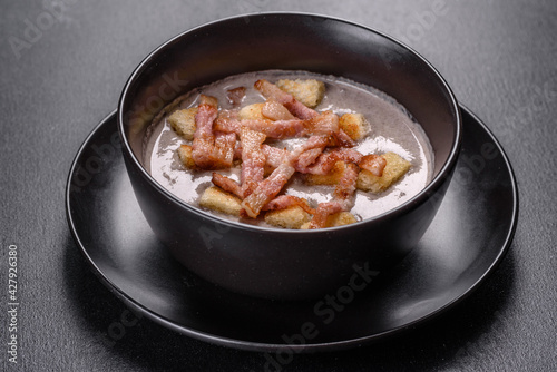 Fresh delicious hot puree soup with mushrooms and bacon in a black plate