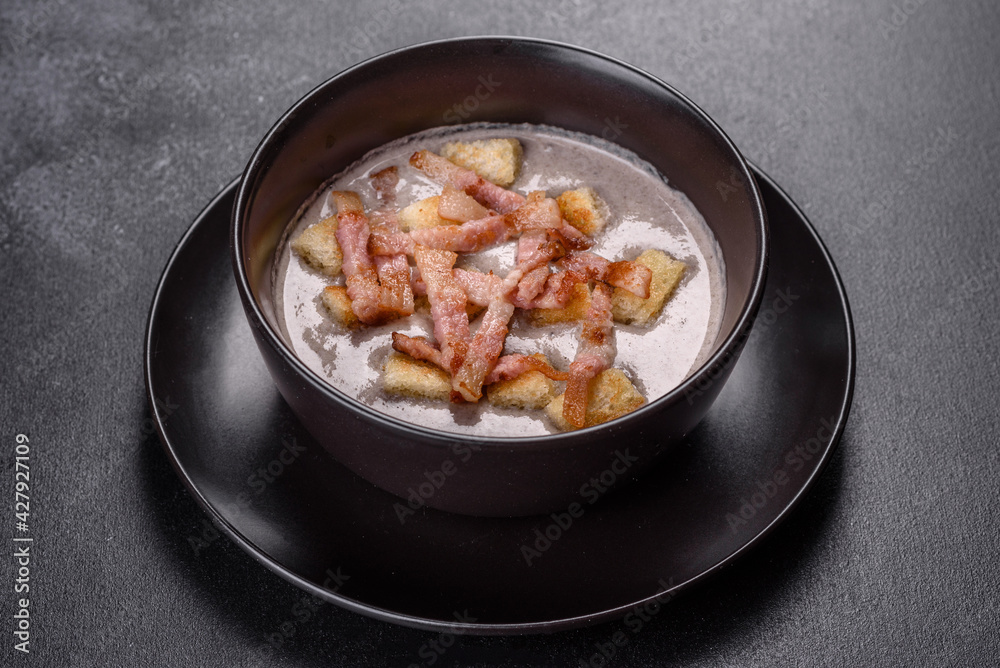 Fresh delicious hot puree soup with mushrooms and bacon in a black plate Fresh delicious hot puree soup with mushrooms and bacon in a black plate