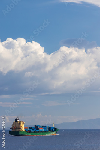 cargo ship nearby Capo Peloro Lighthouse in Punta del Faro on the Strait of Messina, most north eastern promontory of Sicily, Italy photo