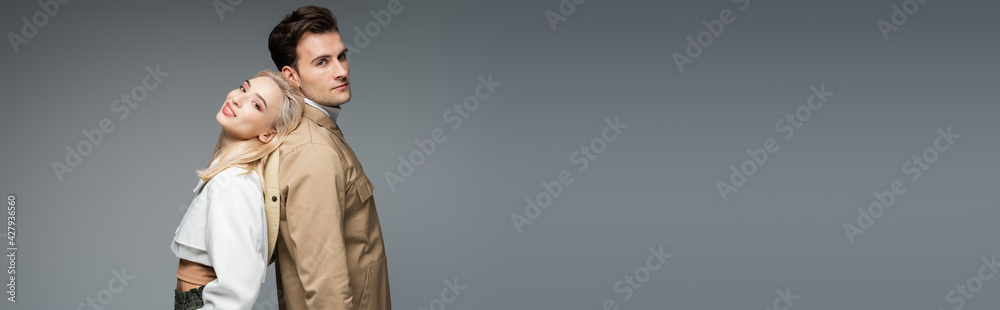 man in jacket standing back to back with cheerful blonde young woman isolated on grey, banner man in jacket standing back to back with cheerful blonde young woman isolated on grey, banner