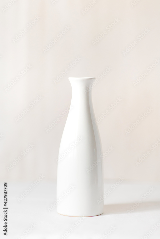 One white vase on a white table. In the background there is a light milky background. One white vase on a white table. In the background there is a light milky background.