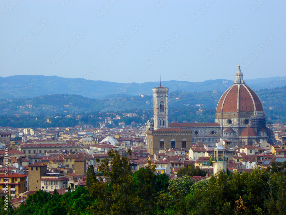 View of the Santa Maria del Fiore cathedral and red rooftop houses in Florence, Italy with Tuscany hills in the background.