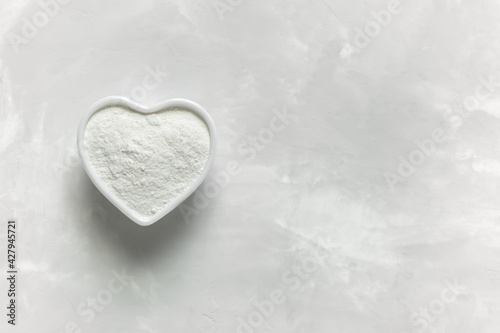 Collagen powder in a white heart-shaped cup on a gray background with a copy space. Natural supplement for health