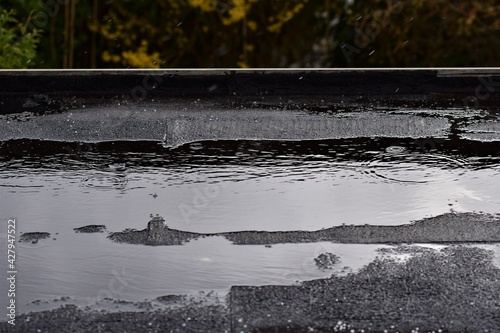 Light rain on a black flat roof against a green background