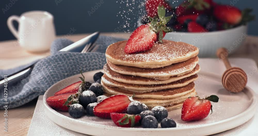 SUPER SLOW MOTION Powdered sugar is being sprinkled over the pancakes pile, served with blueberries and strawberries. Healthy tasty traditional breakfast. Shot with high speed cinema camera