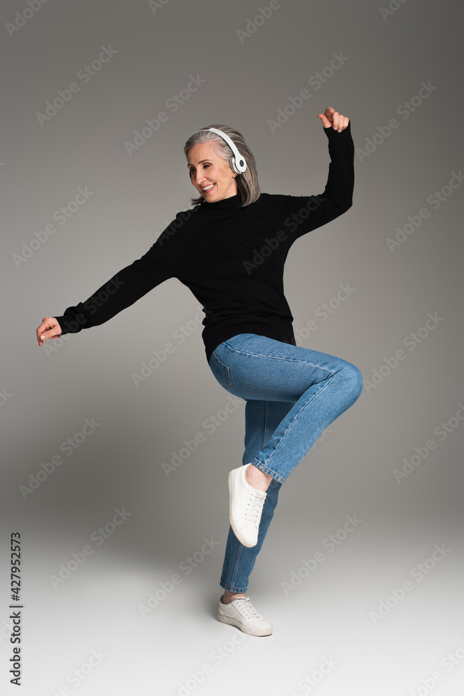 Cheerful woman listening music in headphones on grey background