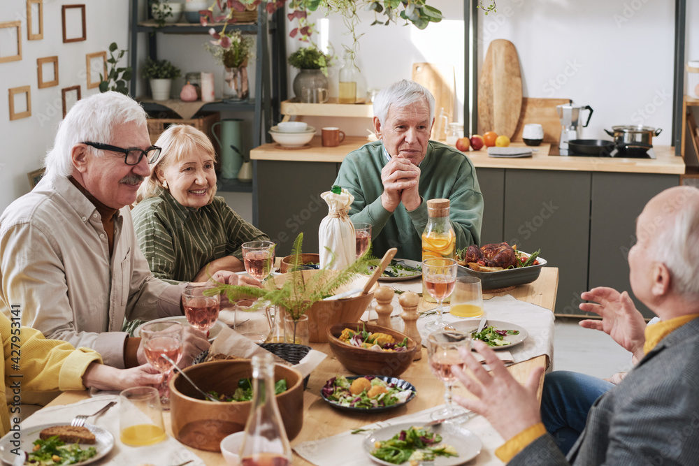 Senior people sitting at dining table and talking to each other during dinner at home Senior people sitting at dining table and talking to each other during dinner at home