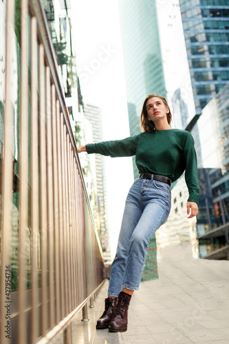 Full length of a hipster girl with short blond hairstyle, wearing in blue, jeans, boots, posing against rough street.
